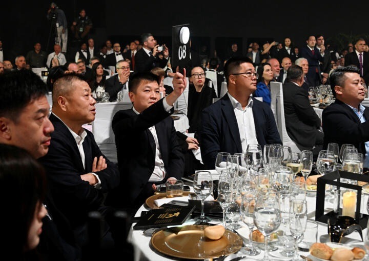 3-1-3 Người tham gia đấu giá nâng bảng số 08 tại sự kiện sang trọng, xung quanh có nhiều người và bàn tiệc.