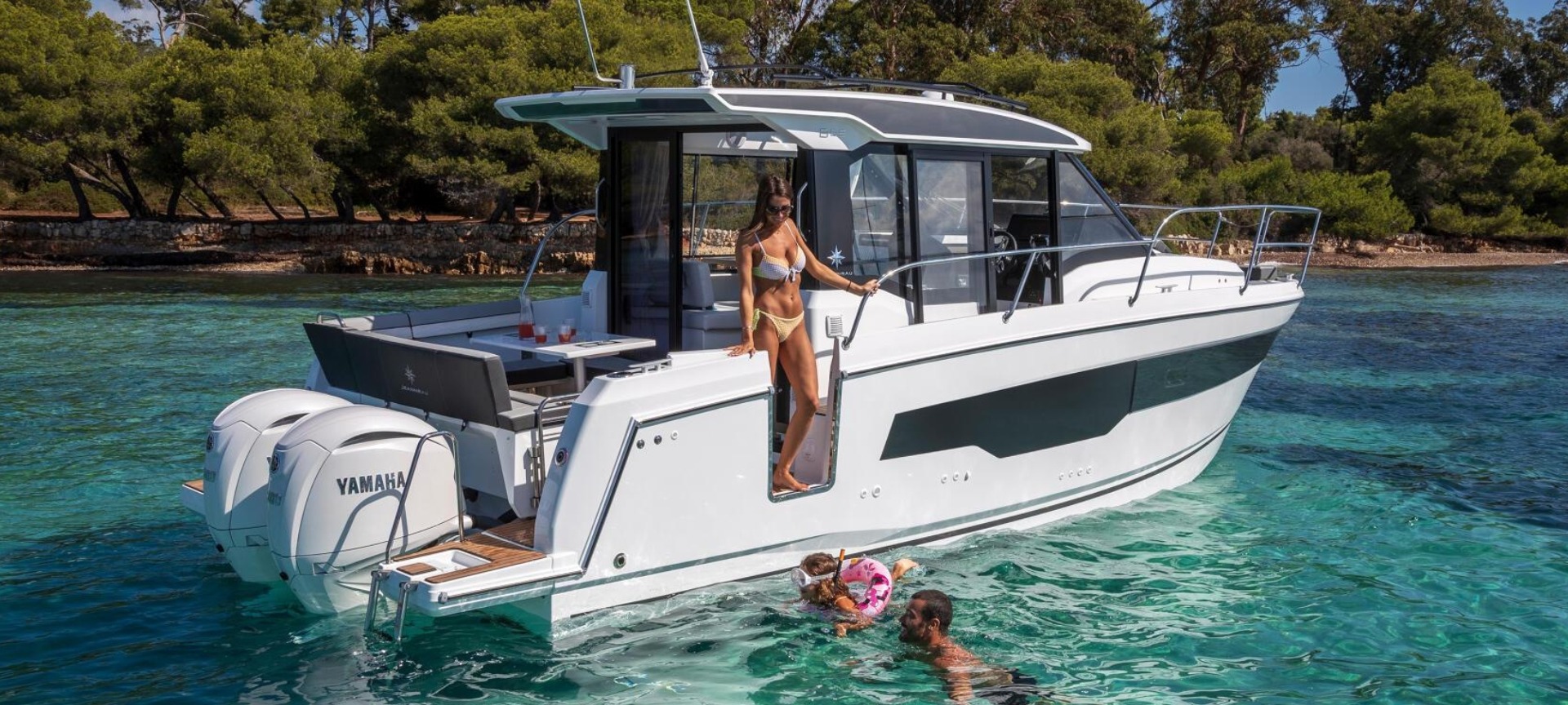 Du thuyền sang trọng trên biển xanh, người phụ nữ tắm nắng, trẻ em và người đàn ông bơi gần bờ.