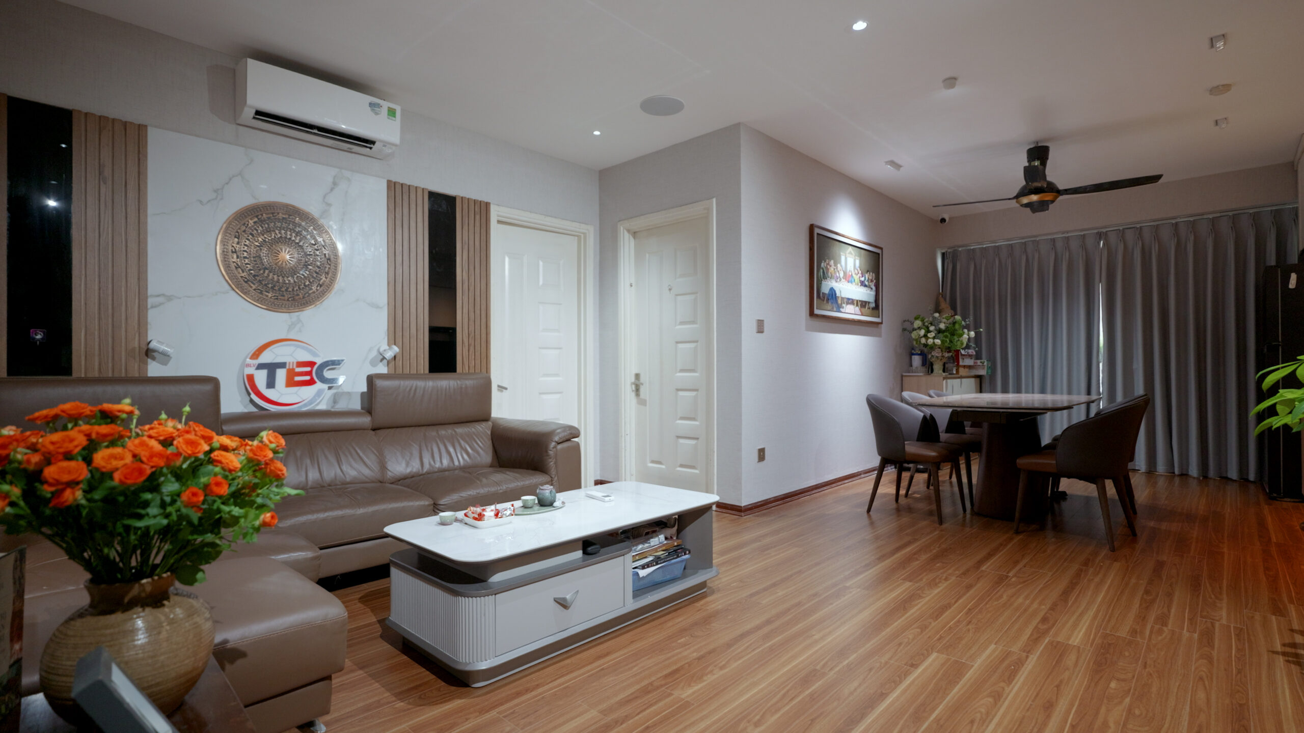 Phòng khách hiện đại với sofa da nâu, bàn trà trắng và bình hoa hồng cam nổi bật.