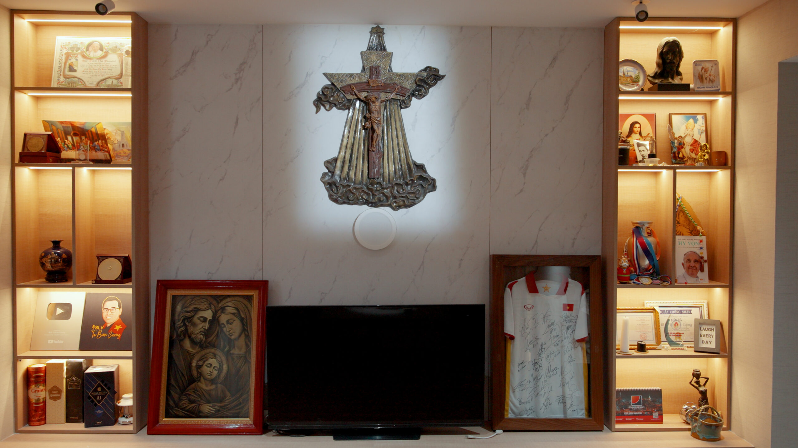 38-scaled-1 Phòng trưng bày với tranh, tượng và áo thể thao ký tên, được chiếu sáng ấm áp, tôn lên bức tượng thánh giá nổi bật.