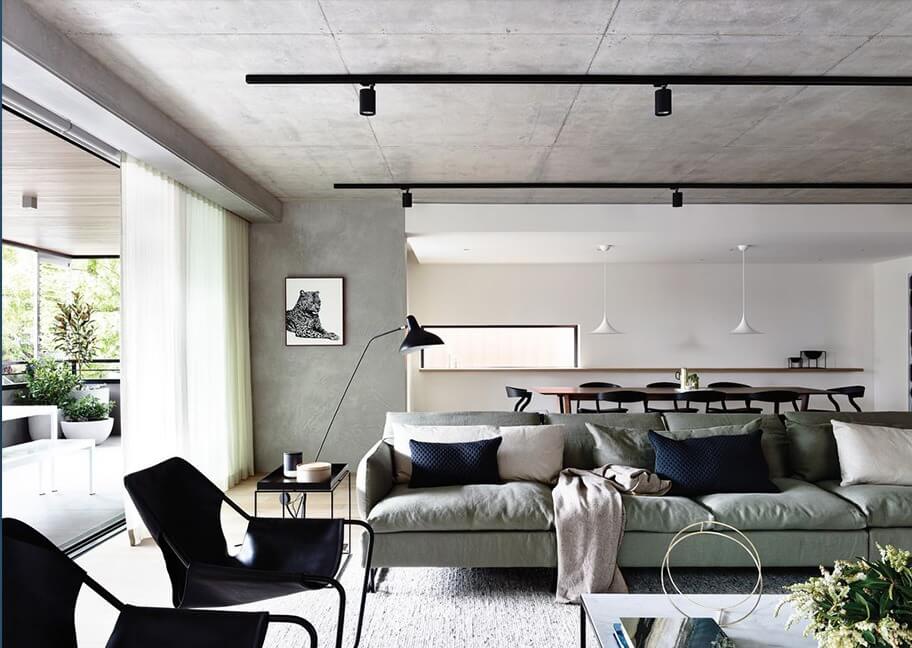 Phòng khách hiện đại với sofa xanh, đèn sàn, bàn kính, và cửa sổ lớn nhìn ra ban công xanh mát.