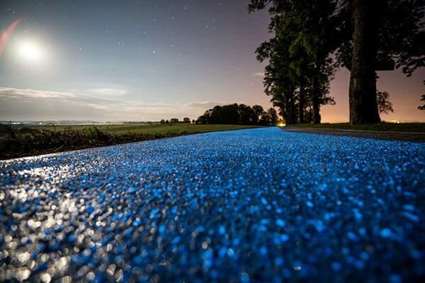 Con đường phát sáng màu xanh dưới ánh trăng và bầu trời đầy sao, được bao quanh bởi cây cối và cánh đồng yên tĩnh.