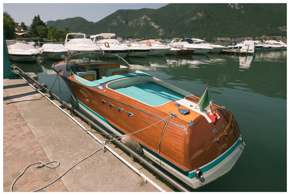 Thuyền gỗ cổ điển neo đậu tại bến cảng, nước xanh mát và dãy núi xanh phía xa, thời tiết nắng đẹp.