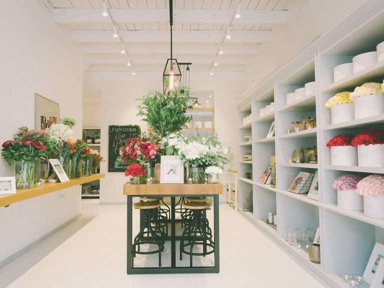 Cửa hàng hoa trang trí hiện đại với nhiều loại hoa tươi được sắp xếp trên kệ và bàn gỗ.