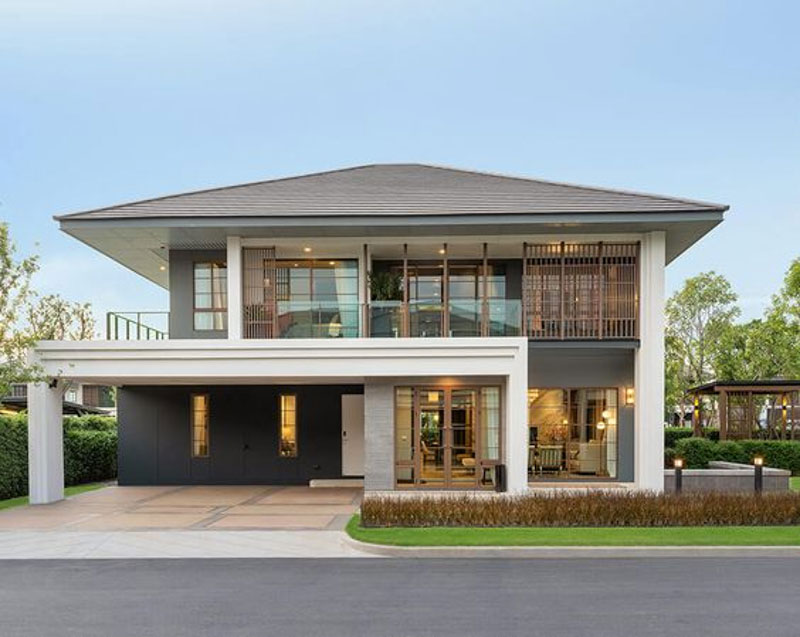 Ngôi nhà hai tầng hiện đại với không gian sân rộng rãi và cửa kính lớn, xung quanh là cây xanh, tạo không gian sống yên bình.