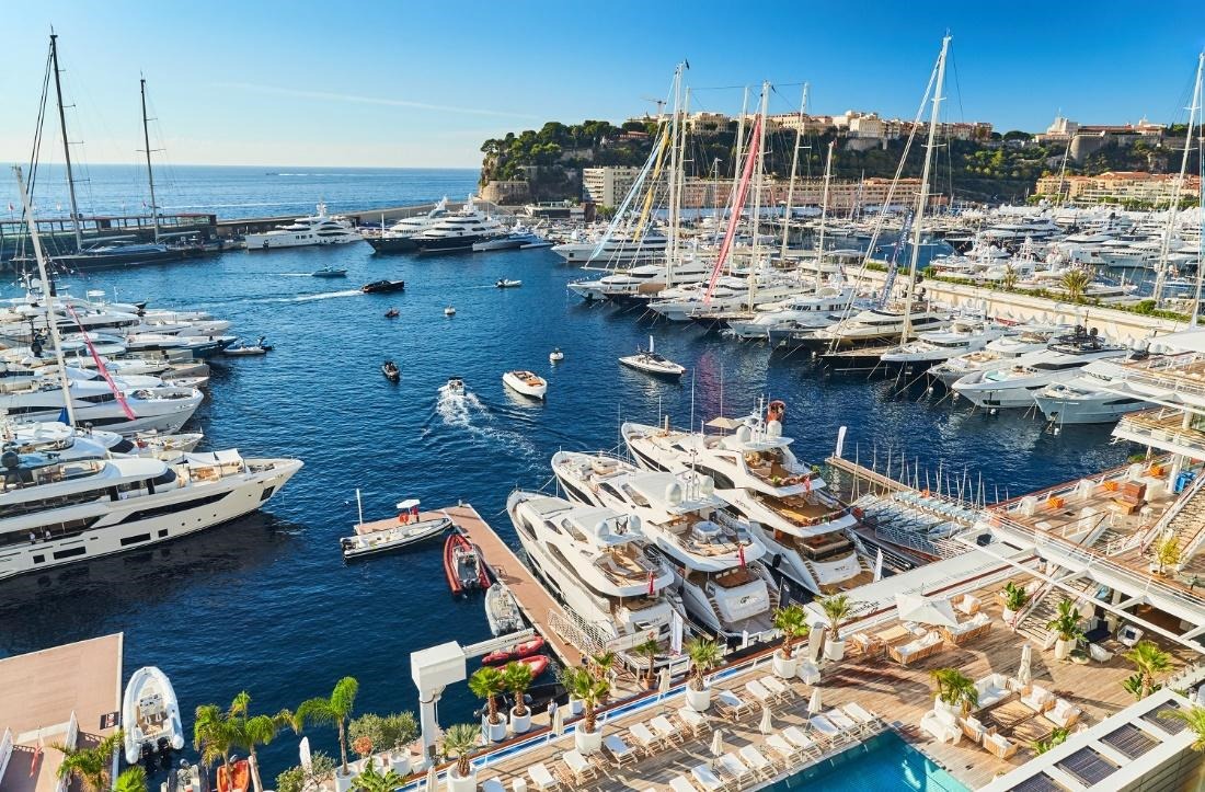 Bến du thuyền Monaco với nhiều du thuyền sang trọng và cảnh quan thiên nhiên đẹp dưới bầu trời trong xanh.