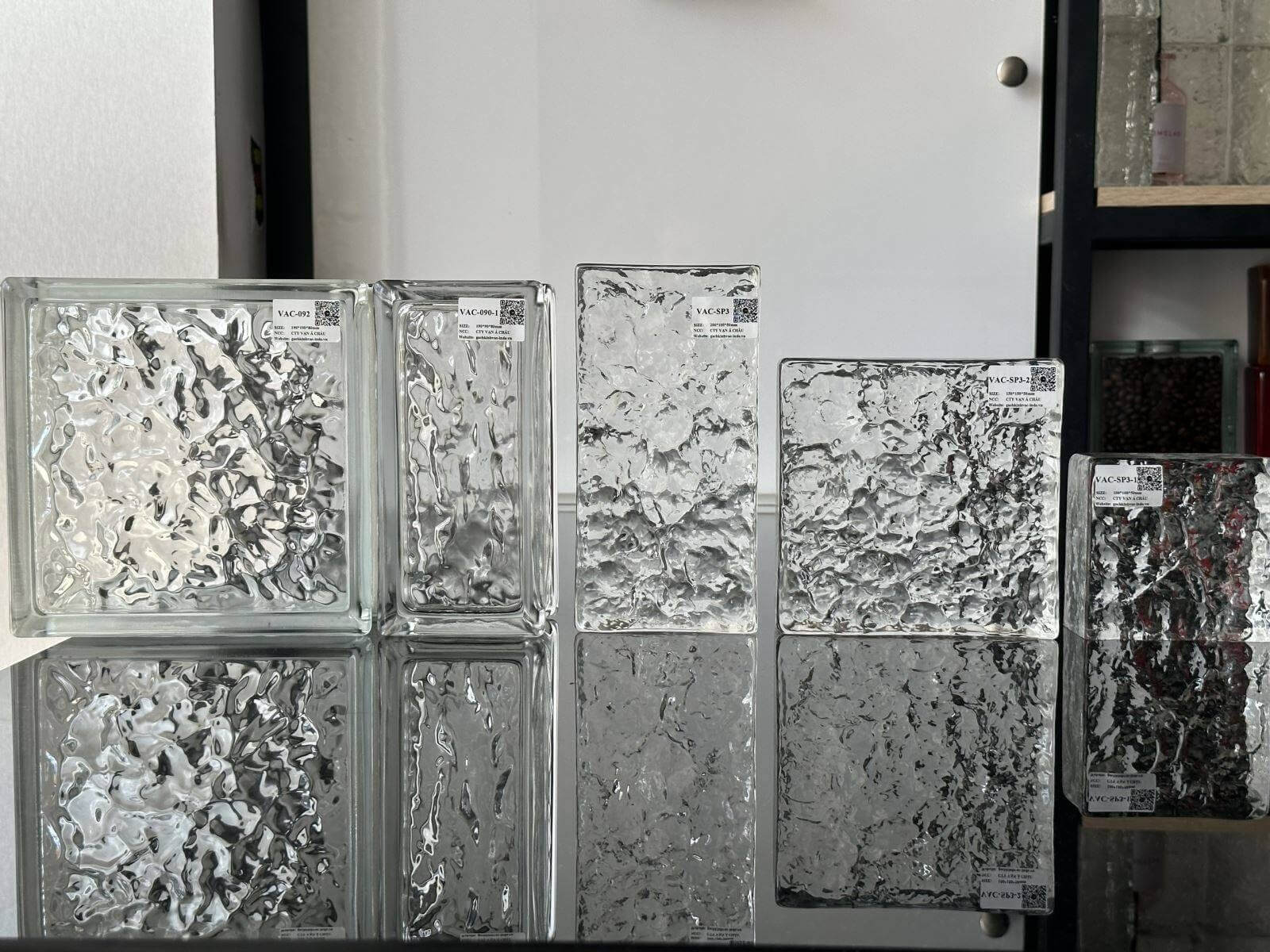 Khối kính hoa văn đặt trên mặt bàn, tạo hình ảnh phản chiếu độc đáo với ánh sáng tự nhiên.