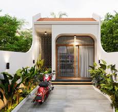 Nhà phố nhỏ hiện đại, mặt tiền với cửa kính lớn và cây xanh xung quanh, xe máy đỗ phía trước.