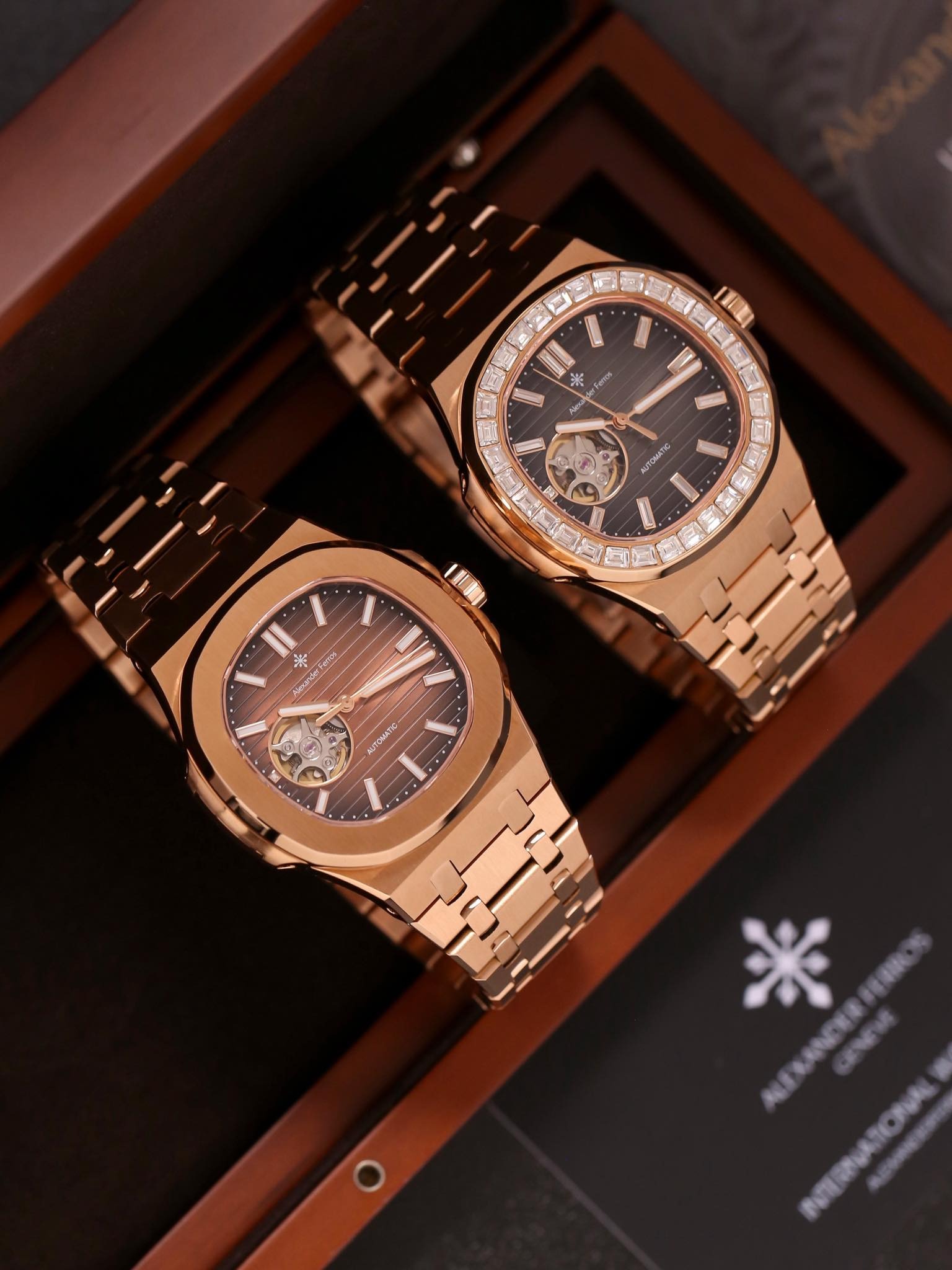 Cặp đồng hồ đeo tay vàng hồng sang trọng trên nền hộp gỗ, mặt số đen với thiết kế lộ máy tinh tế.