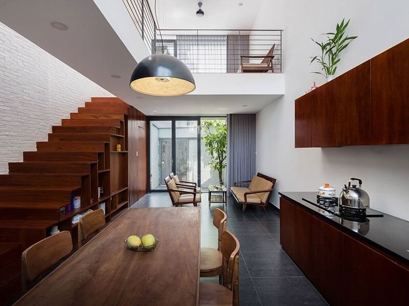 Phòng khách hiện đại với bàn gỗ, cầu thang gỗ, ánh sáng tự nhiên và cây xanh trang trí.