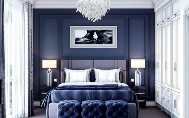 Phòng ngủ sang trọng với tông màu xanh đậm, giường nệm êm ái và ánh sáng chùm đèn hiện đại.