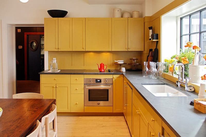 Nhà bếp hiện đại với tủ màu vàng, bàn đá và trang trí hoa tạo cảm giác ấm cúng và sáng sủa.