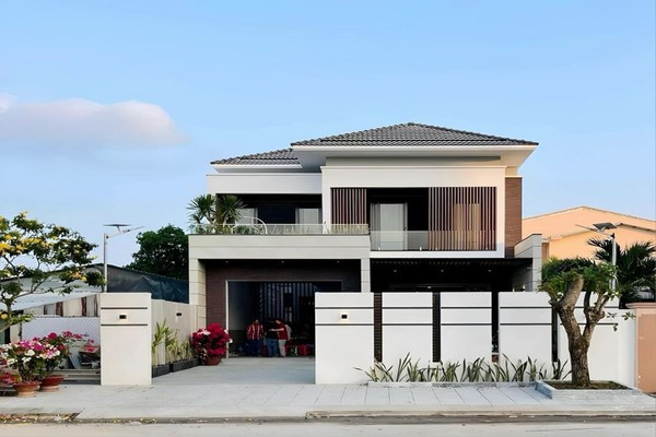 Ngôi nhà hiện đại hai tầng với mái ngói, sân rộng và cây cảnh, trời xanh trong dịu nhẹ.