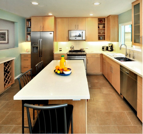 Nhà bếp hiện đại với tủ gỗ, bàn đảo, tủ lạnh, lò vi sóng, và chậu rửa, ánh sáng tự nhiên qua cửa sổ.