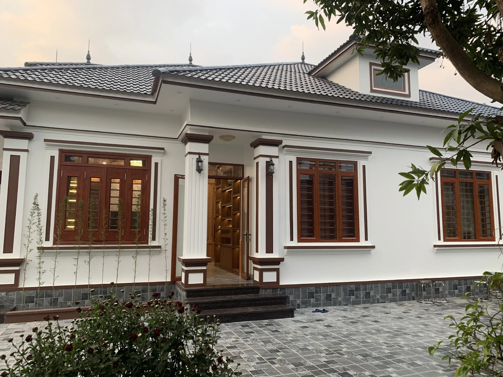 Ngôi nhà mái ngói hiện đại với cửa gỗ, sân lát đá và cây xanh tạo không gian thoáng đãng.