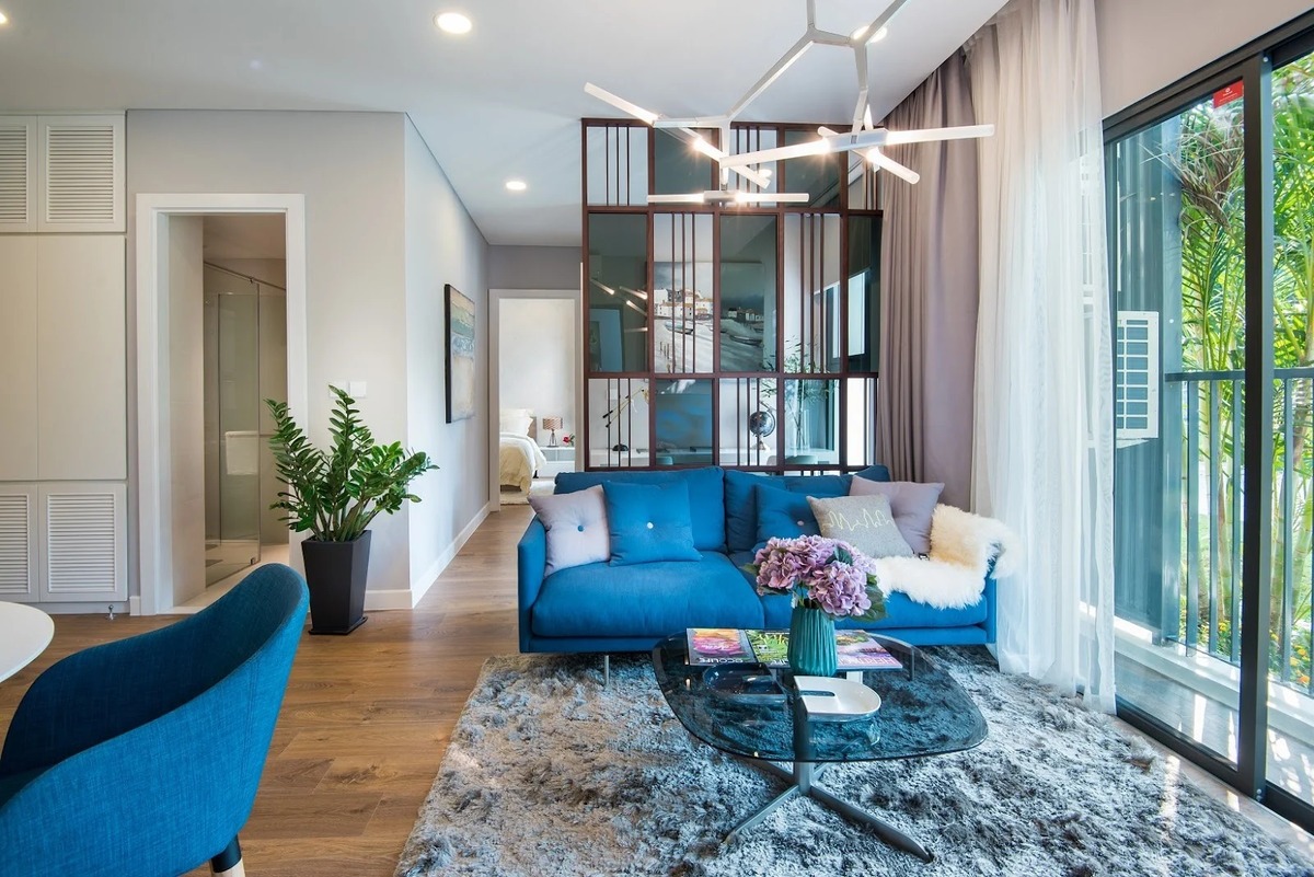 Phòng khách hiện đại với sofa xanh, bàn kính và cây cảnh trong căn hộ sáng sủa.