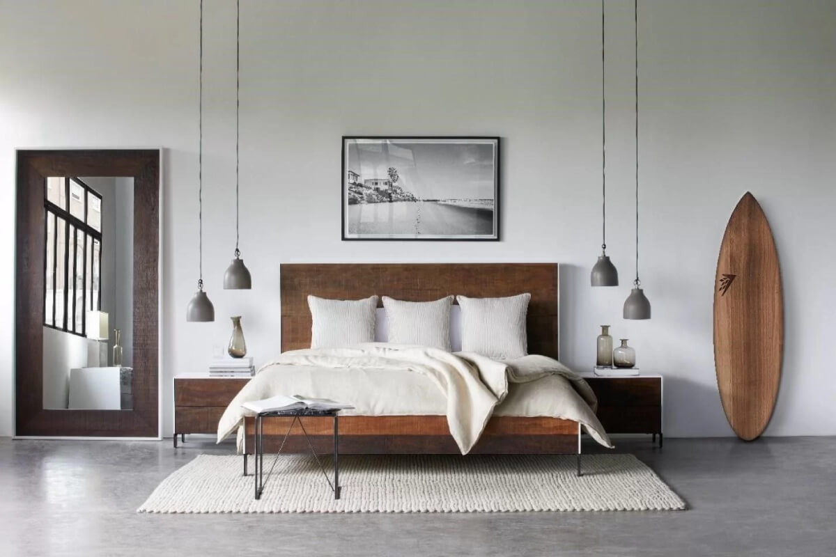 Phòng ngủ hiện đại với giường gỗ, bảng lướt sóng, đèn thả, và tranh treo tường trắng đen.