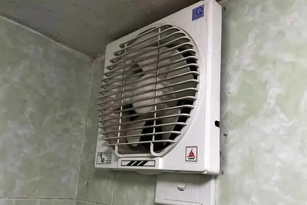 Quạt thông gió gắn tường màu trắng đang hoạt động trong phòng với tường nền màu xanh nhạt.