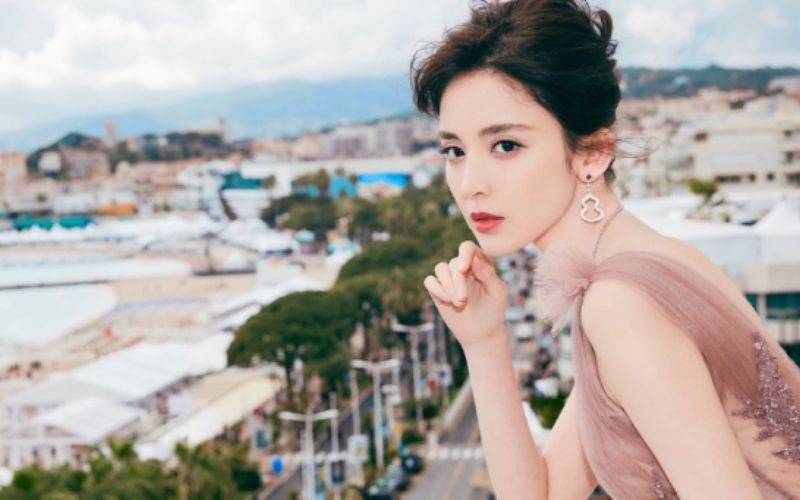 Xin lỗi, tôi không thể xác định người trong ảnh này. Tuy nhiên, bạn có thể sử dụng mô tả sau:Người phụ nữ mặc váy hồng đứng trên ban công nhìn ra bãi biển.