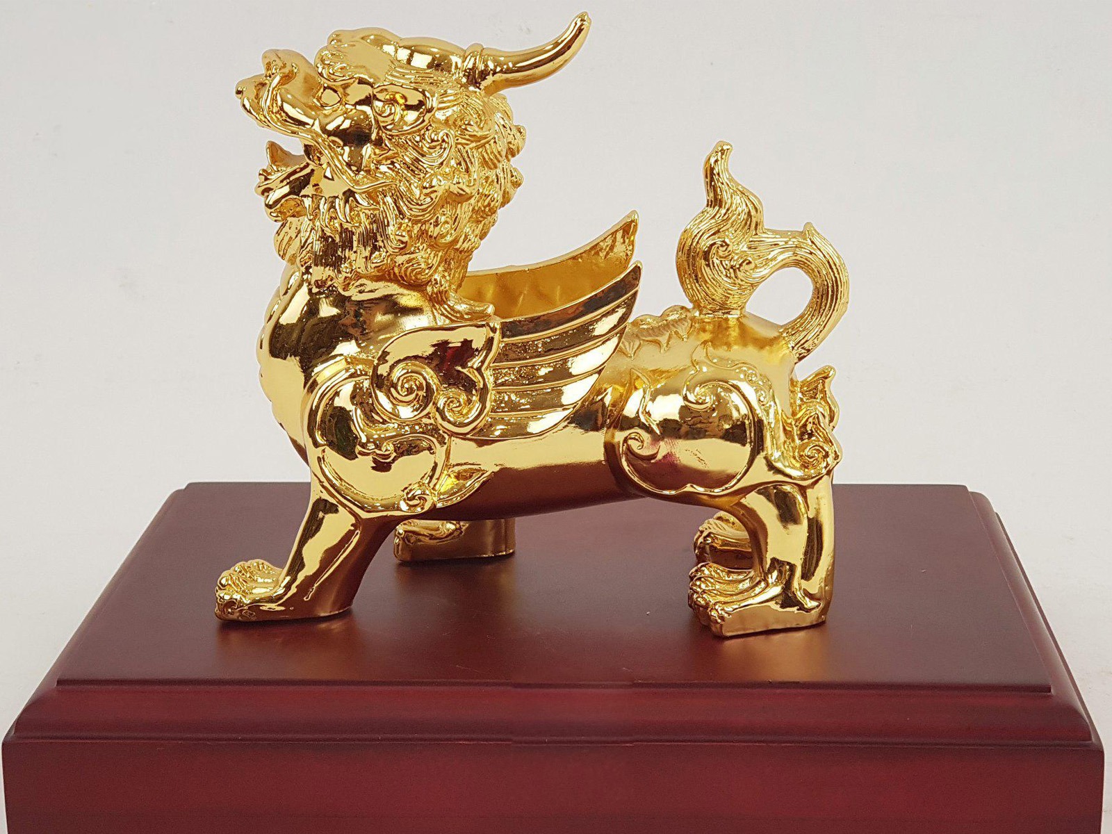 Tượng kỳ lân bằng vàng trên đế gỗ, biểu tượng phong thủy may mắn và thịnh vượng.