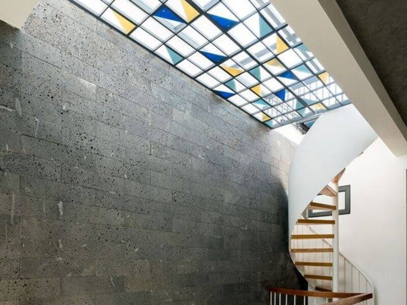 Cầu thang xoắn hiện đại dưới trần kính màu hình tam giác, tạo ánh sáng nghệ thuật cho không gian sống.