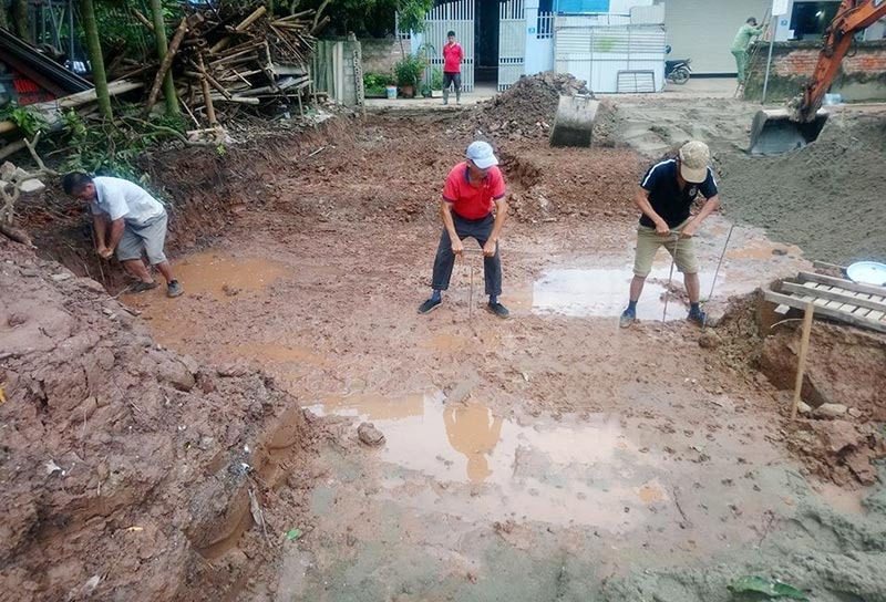 Ba người đàn ông đang đào đất tại công trường xây dựng, bùn lầy và vũng nước xung quanh.