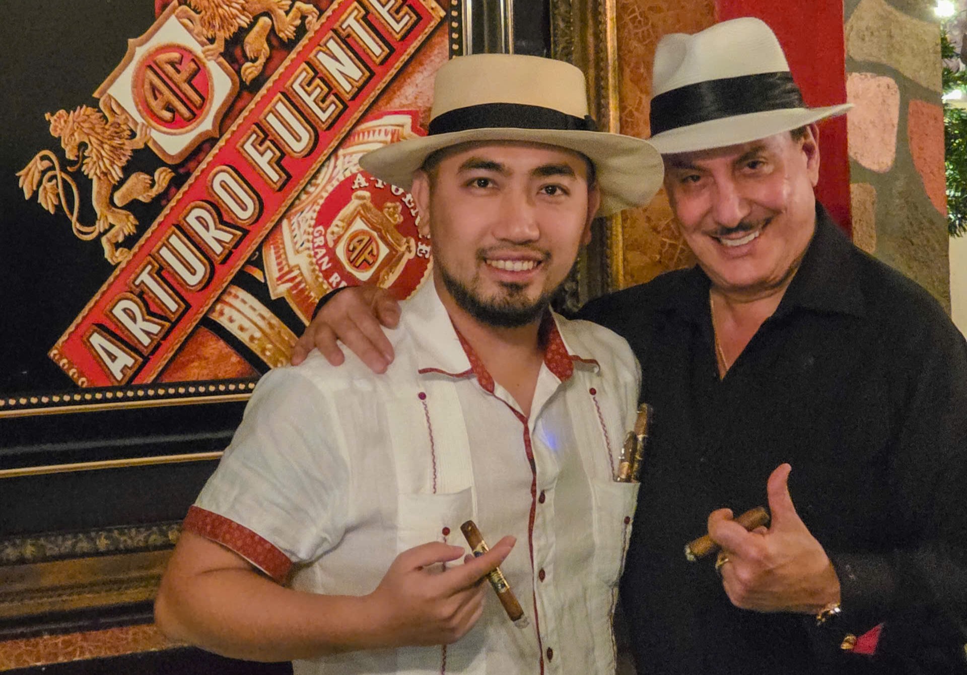 anh-khoac-vai-ngang-2 Hai người đàn ông đội mũ Panama cầm xì gà trước bảng hiệu Arturo Fuente.