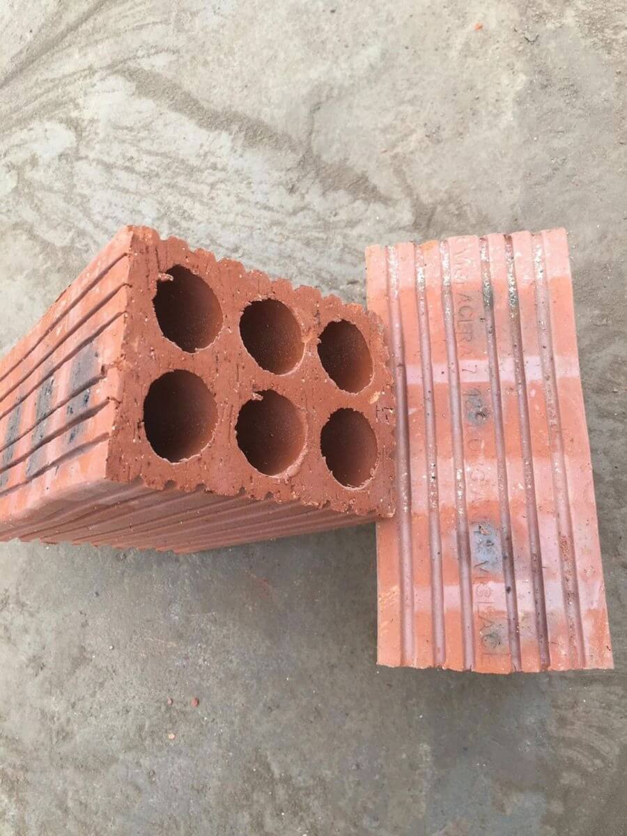 Gạch xây dựng màu đỏ với sáu lỗ tròn trên bề mặt, đặt trên nền xi măng.