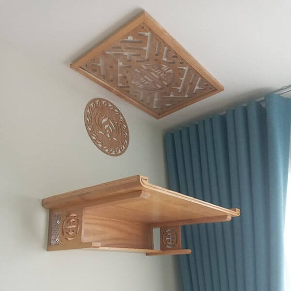 Kệ thờ gỗ treo tường với thiết kế hoa văn tinh tế, rèm xanh phía sau tạo không gian trang nhã.