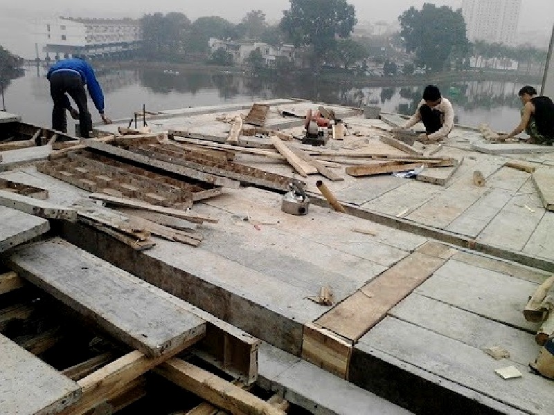 bao-duong-nghiem-thu-va-thao-cop-pha Công nhân xây dựng đang làm việc trên sàn bê tông gần hồ, xung quanh có nhiều mảnh gỗ và công cụ xây dựng.