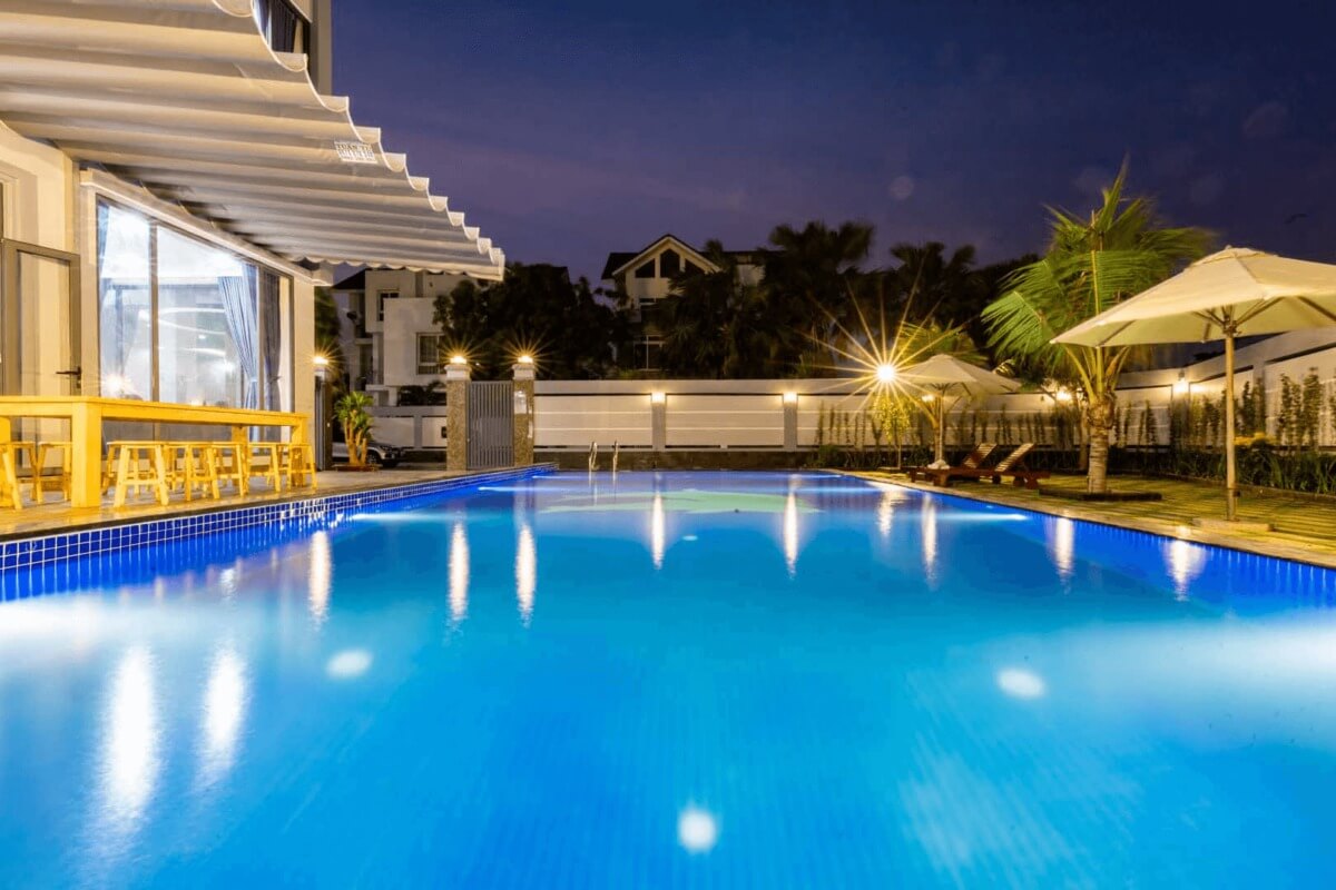 Hồ bơi ngoài trời lung linh vào buổi tối, với ánh đèn và cây cọ tạo không gian thư giãn lý tưởng.
