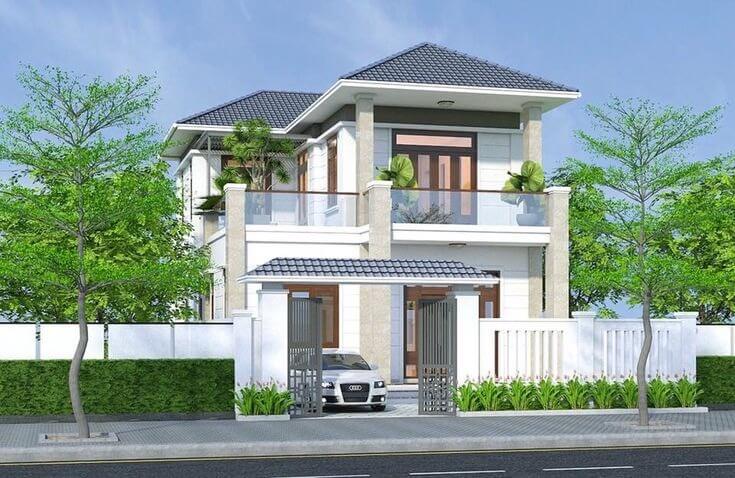 Nhà biệt thự hiện đại 2 tầng, mái ngói xanh, sân vườn rộng rãi với cây xanh, hàng rào trắng và ô tô đỗ trước cửa.