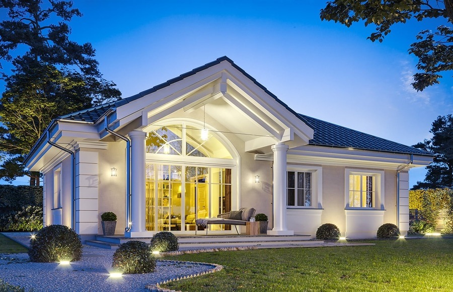 Nhà hiện đại với cửa kính lớn, sân vườn thoáng đãng, chiếu sáng ban đêm, mái ngói sang trọng, cây xanh bao quanh.