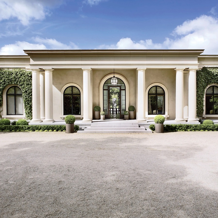 Mặt tiền biệt thự sang trọng với cột lớn, cửa sổ vòng cung và cây xanh tạo điểm nhấn kiến trúc.