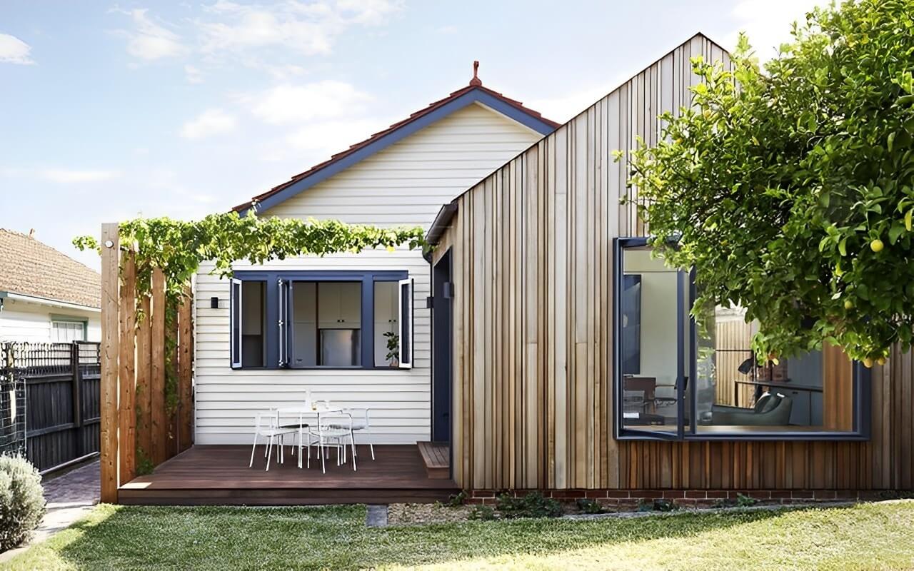 Nhà gỗ và sân vườn xanh tươi, ban công nhỏ với bàn ghế trắng, thiết kế hiện đại, ánh sáng tự nhiên.