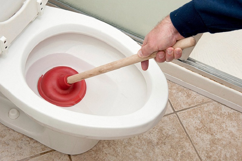 Người dùng sử dụng cây thông bồn cầu để thông tắc toilet trong phòng vệ sinh.
