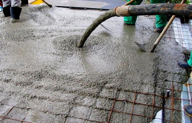 Công nhân đổ bê tông tươi trên mặt sàn xây dựng, với lưới thép gia cố bên dưới.