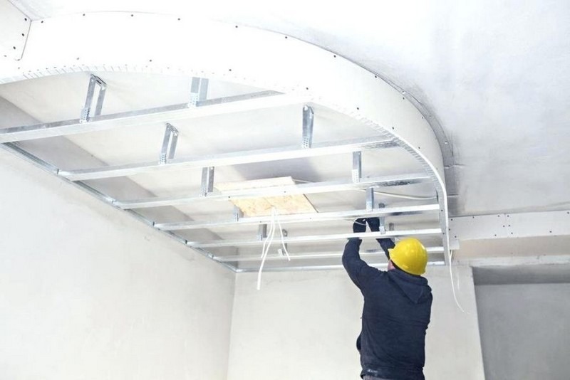 Công nhân xây dựng lắp ráp hệ thống trần thạch cao trong nhà, đang đeo mũ bảo hộ màu vàng.