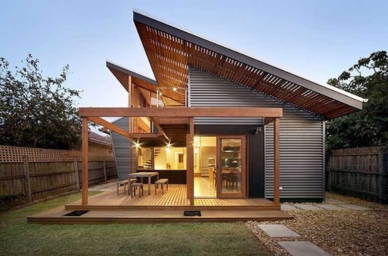 Nhà hiện đại với mái chéo và sân gỗ, cửa kính lớn, không gian mở, thiết kế sáng tạo giữa thiên nhiên.