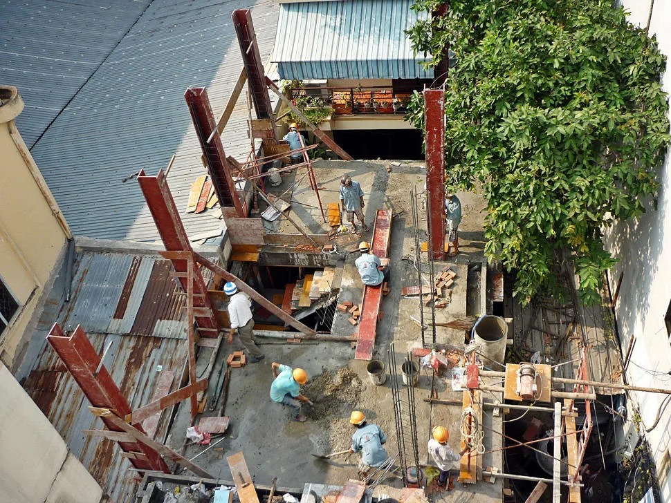 Công nhân xây dựng đang làm việc tại công trường với các cột thép và cát, nhìn từ trên cao.