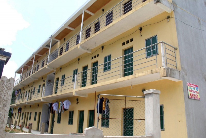 Khu nhà trọ 3 tầng với ban công và cửa sổ xanh lá, bên ngoài có quần áo treo phơi.