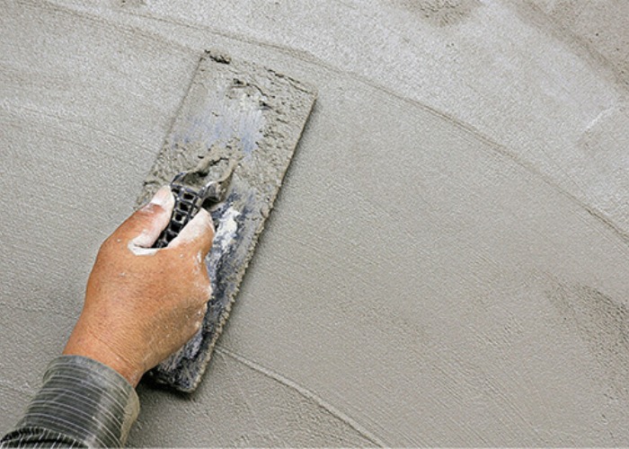 Tay thợ xây sử dụng bay để trát xi măng lên tường, làm mịn bề mặt xây dựng.