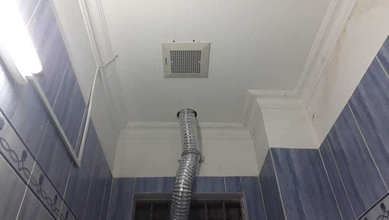 Hệ thống thông gió trên trần phòng tắm với ống dẫn bằng kim loại và gạch ốp tường xanh.