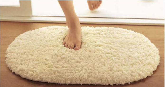Bàn chân đi trên thảm chùi chân màu trắng hình bầu dục mềm mại đặt trên sàn gỗ gần cửa.