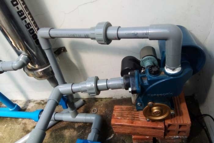 Máy bơm nước màu xanh lắp đặt với ống nhựa PVC trong không gian nội thất.