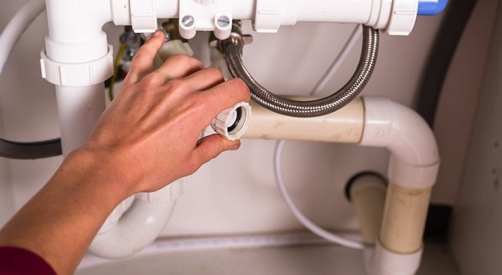 Bàn tay sửa chữa ống nước dưới bồn rửa, bảo dưỡng hệ thống ống dẫn nước trong nhà.