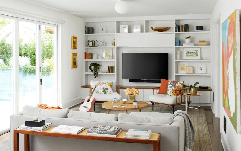 Phòng khách hiện đại với kệ sách, ghế sofa màu xám, trang trí cây xanh và tivi màn hình phẳng.