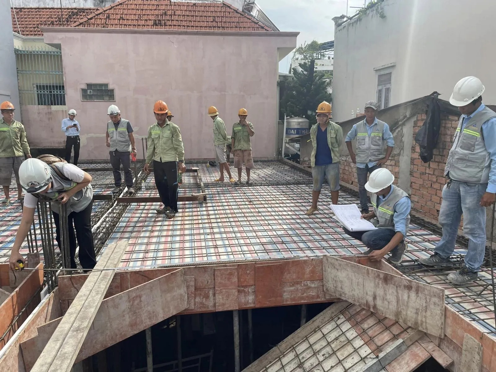 Nhóm công nhân xây dựng kiểm tra công trình tại công trường, đội mũ bảo hộ và vẽ thiết kế.