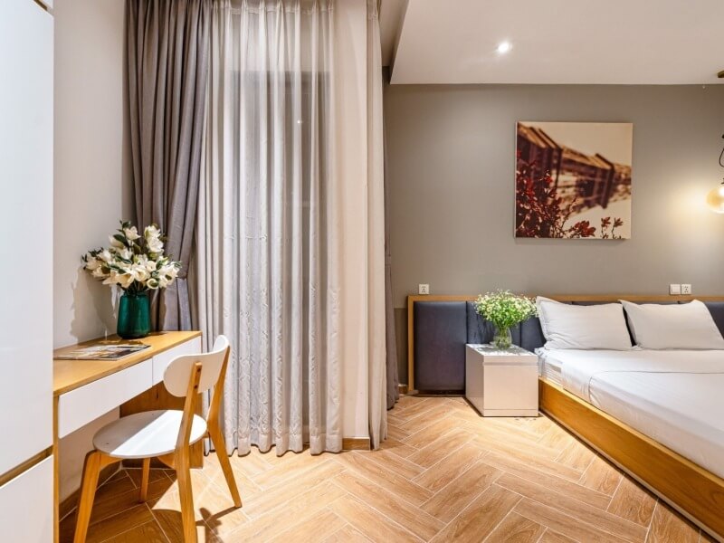 Phòng ngủ hiện đại với giường đôi, bàn làm việc, rèm cửa và tranh treo tường.