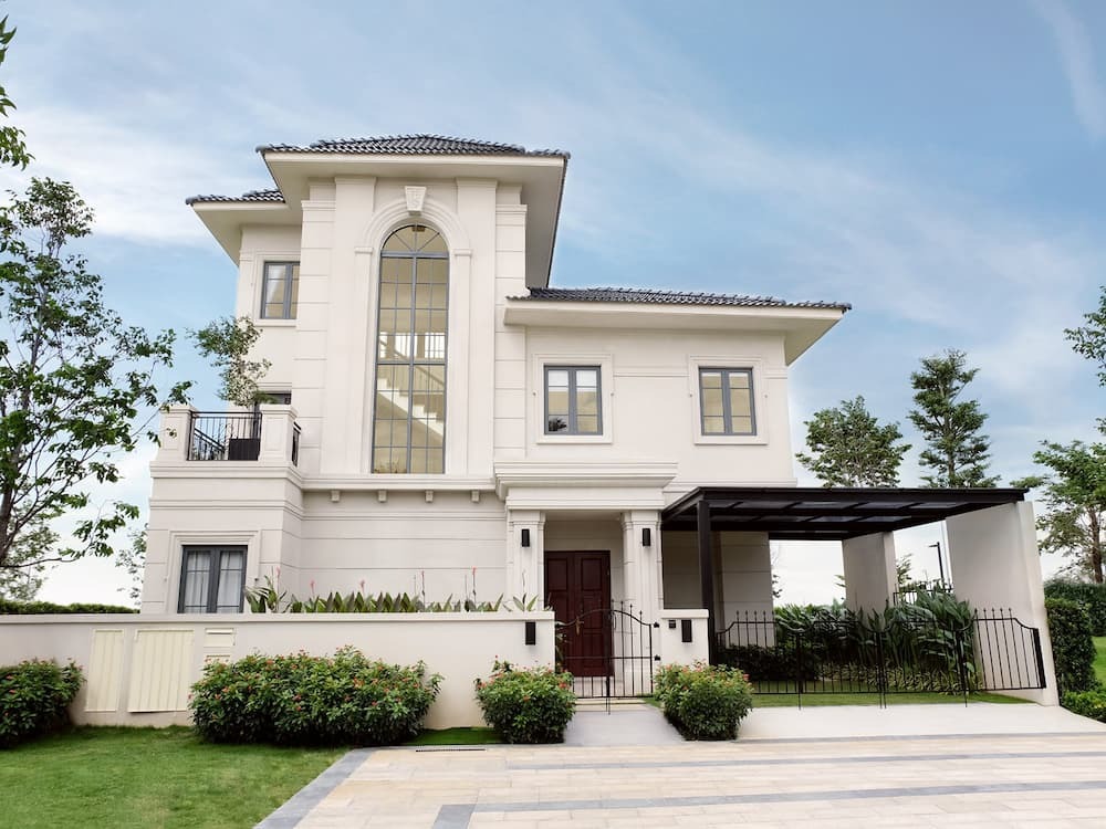 Mặt tiền biệt thự hiện đại với mái ngói và sân vườn xanh tươi, giữa không gian rộng lớn và bầu trời xanh.
